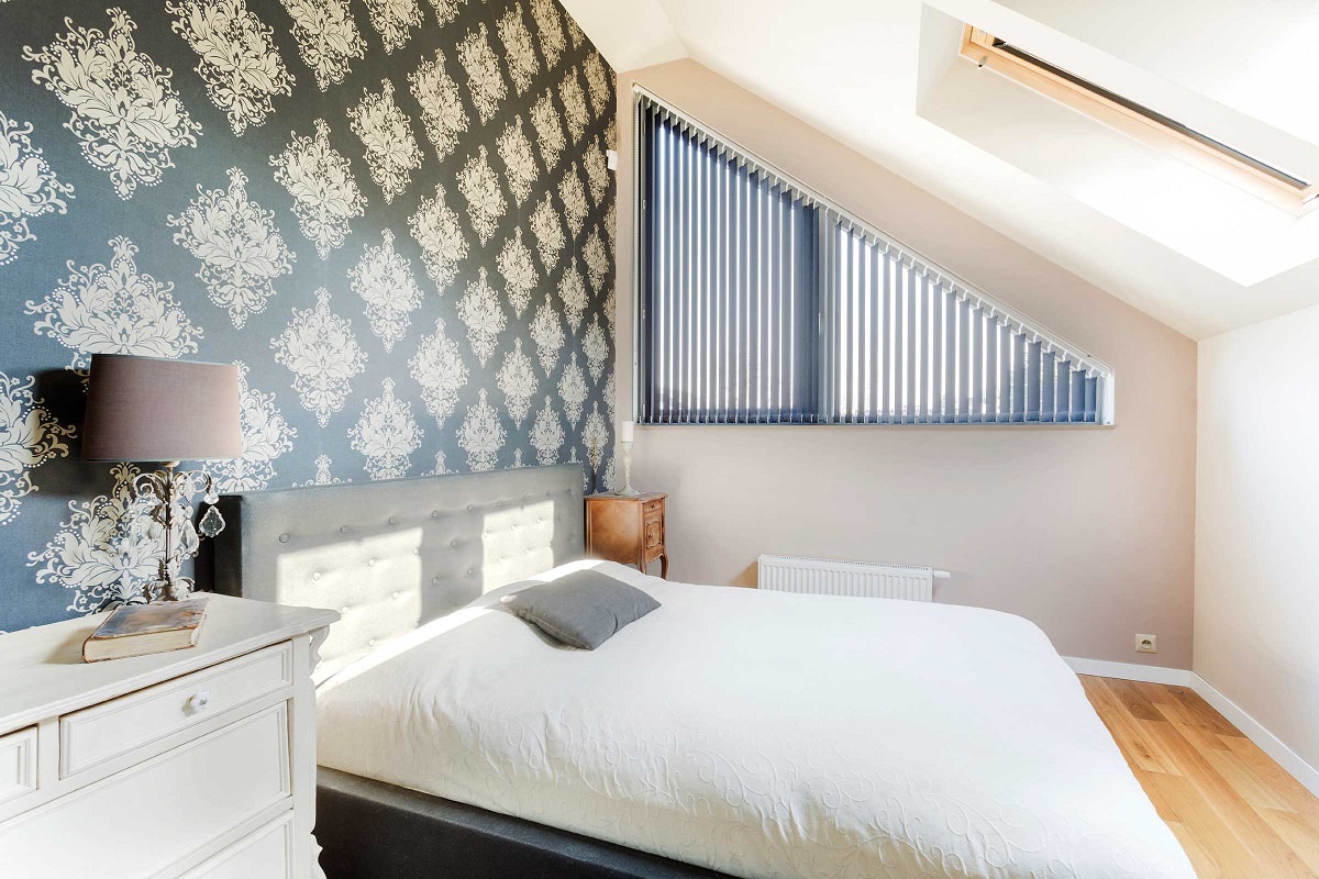 اتاق خوابی که به دیوار پشت تخت آن کاغذ دیواری سیاه نصب شده است و باقی دیوارها به رنگ خنثی نقاشی شده است